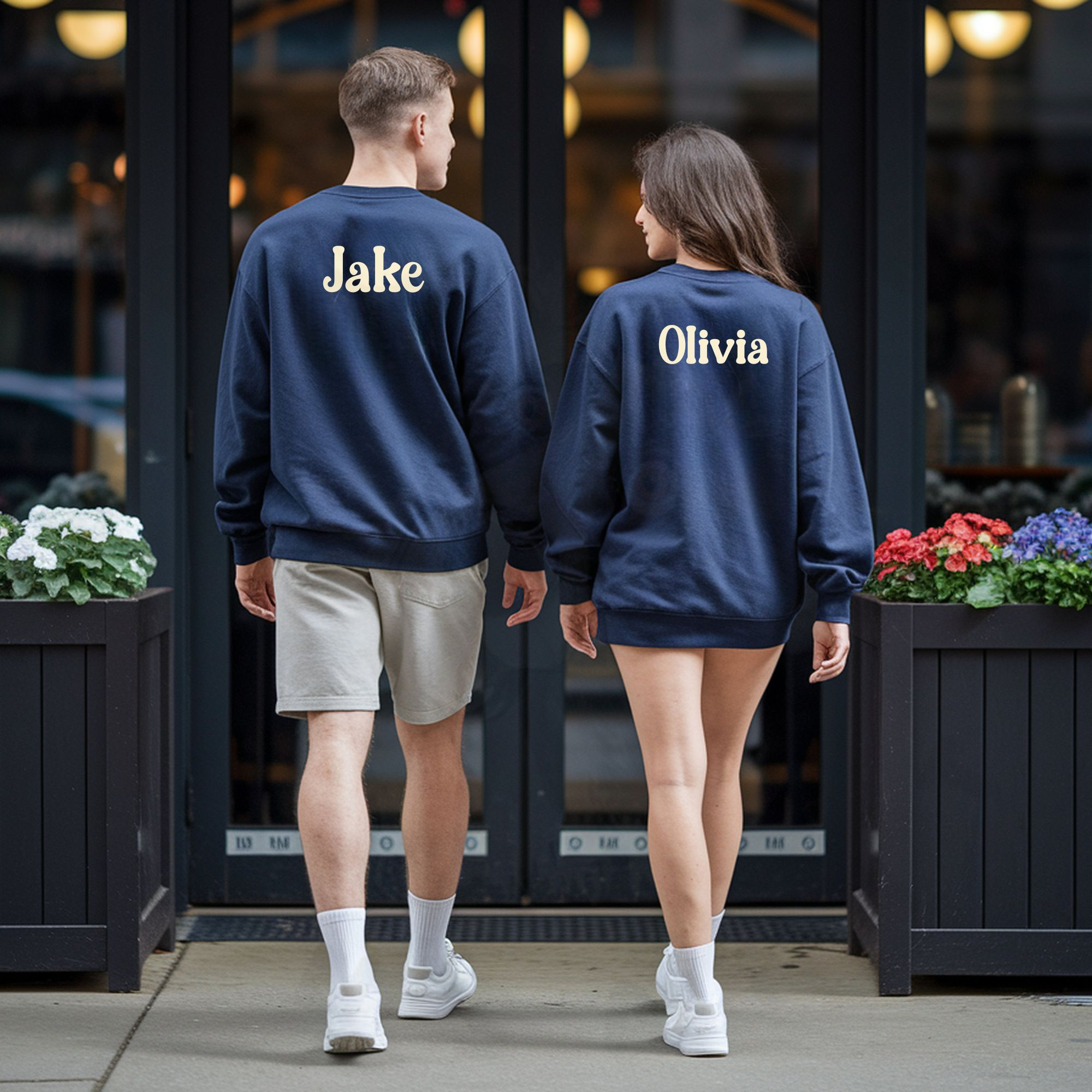 a man and woman walking away from the camera and into a restaurant wearing navy blue sweatshirts with their names on the back