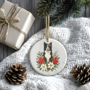 a stylized christmas scene of a package, pine cones, greenery, and a blanket with a round ceramic christmas ornament featuring a graphic of christmas flowers and greenery surrounding a border collie