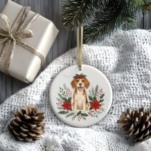 a stylized christmas scene of a package, pine cones, greenery, and a blanket with a round ceramic christmas ornament featuring a graphic of christmas flowers and greenery surrounding a beagle