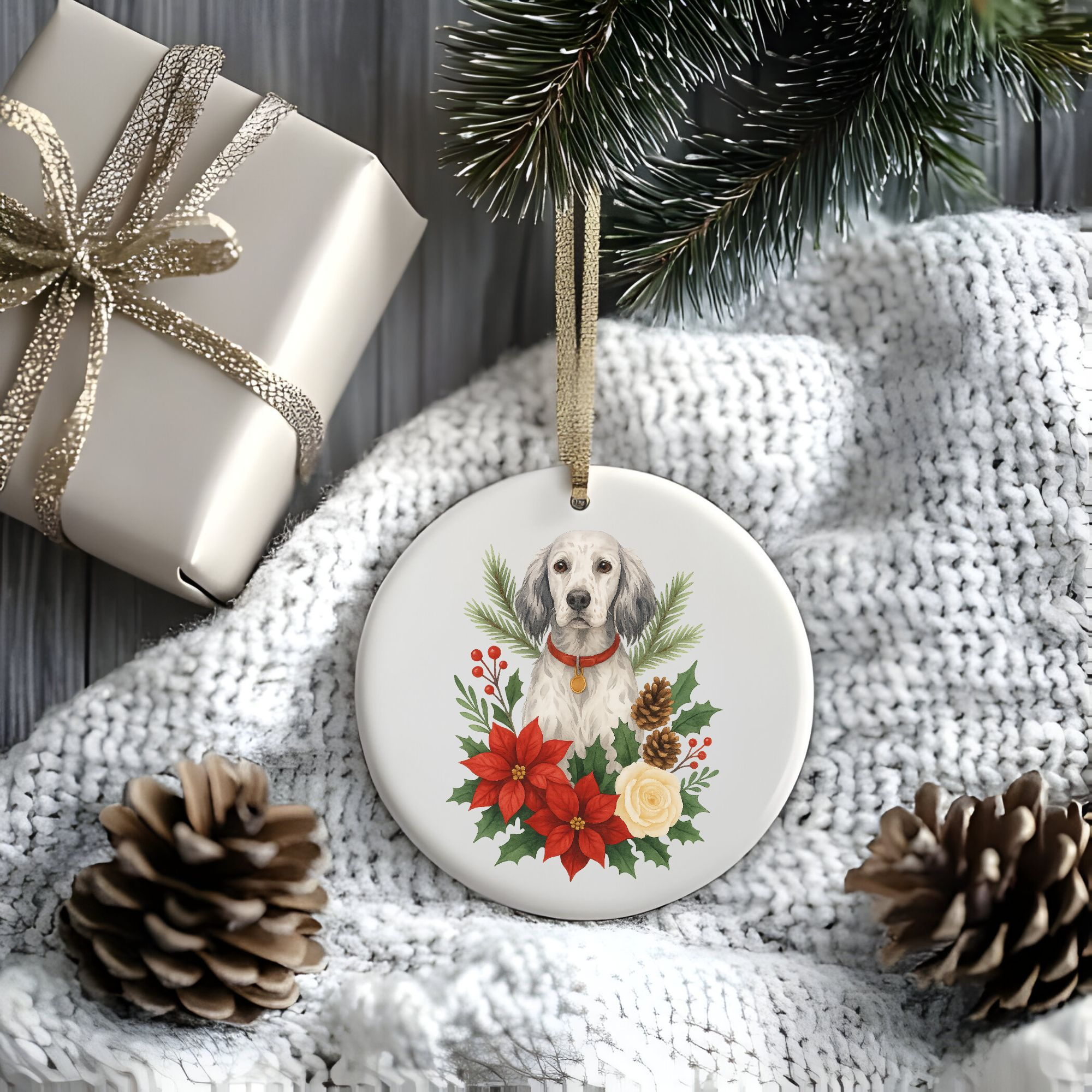 a stylized christmas scene of a package, pine cones, greenery, and a blanket with a round ceramic christmas ornament featuring a graphic of christmas flowers and greenery surrounding an english setter