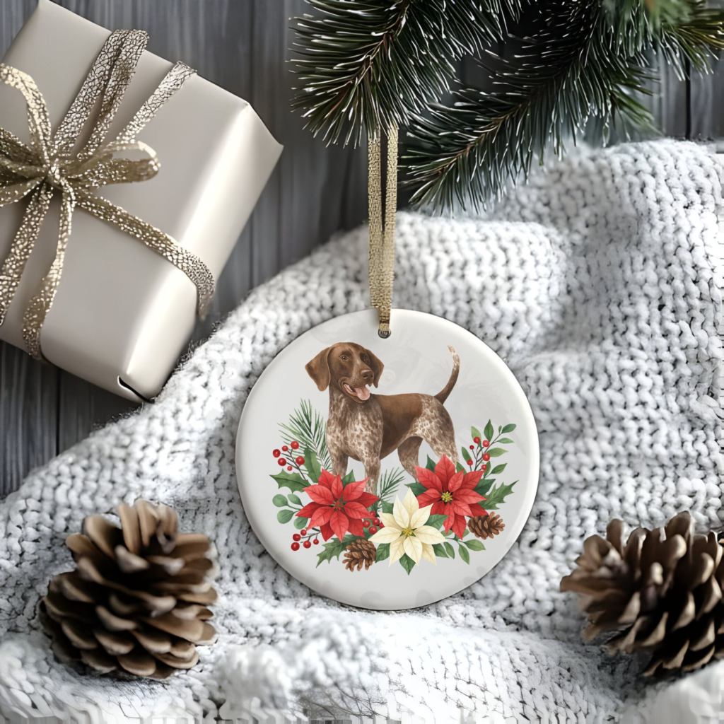 a stylized christmas scene of a package, pine cones, greenery, and a blanket with a round ceramic christmas ornament featuring a graphic of christmas flowers and greenery surrounding a german shorthair pointer
