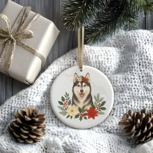 a stylized christmas scene of a package, pine cones, greenery, and a blanket with a round ceramic christmas ornament featuring a graphic of christmas flowers and greenery surrounding a husky