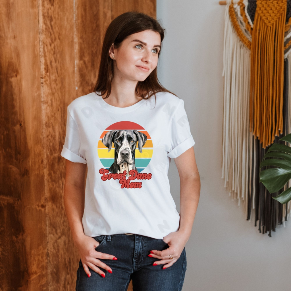 a woman wearing a white tee featuring a retro sunset design with a great dane and the words great dane mom in retro script
