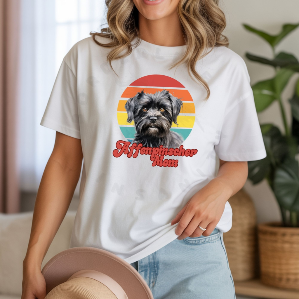 A woman wearing a white tee featuring a retro sunset design that says Affenpinscher mom tee