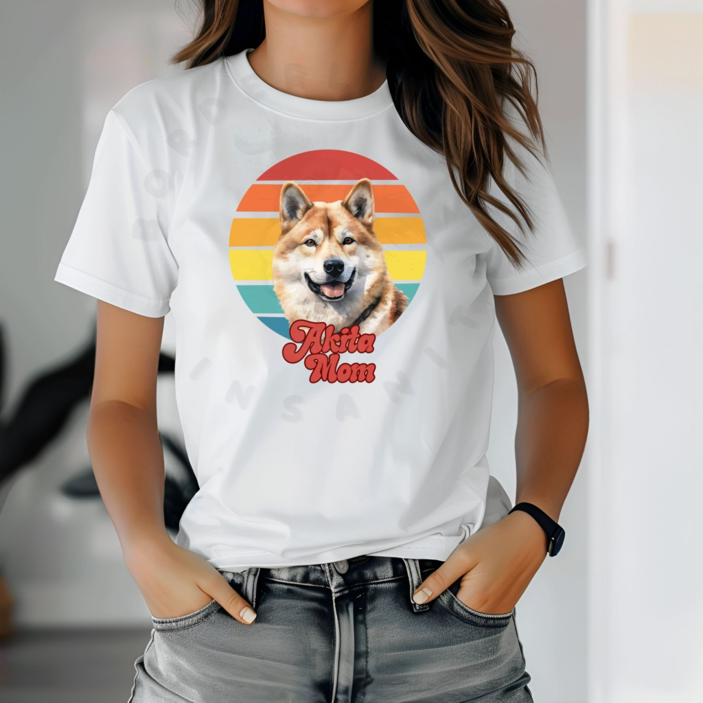 a woman with her hands in her pockets wearing a white tee with a retro sunset design featuring an akita and the words akita mom in retro script