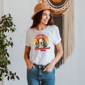 a woman wearing a white tee featuring a retro sunset design with a basset hound and the words basset hound mom in retro script