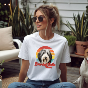 a woman wearing a white tee featuring a retro sunset design with a bearded collie and the words bearded collie mom in retro script