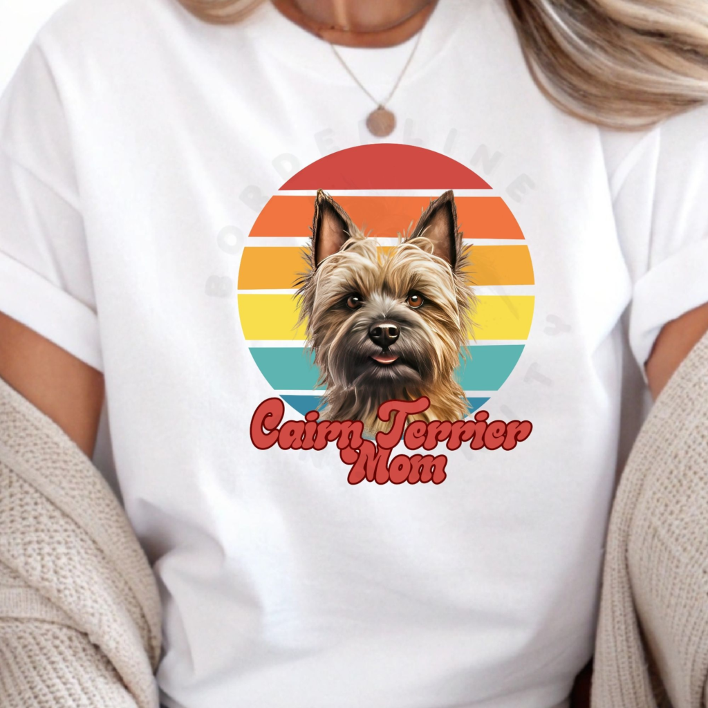 a woman wearing a white tee featuring a retro sunset design and a cairn terrier with the words cairn terrier mom in retro script