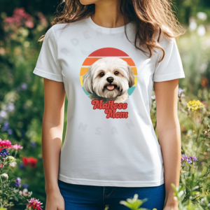 a woman wearing a white tee featuring a retro sunset design with a maltese and the words maltese mom in retro script