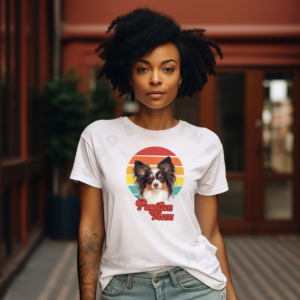 a woman wearing a white tee featuring a retro sunset design with a papillon and the words papillon mom in retro script