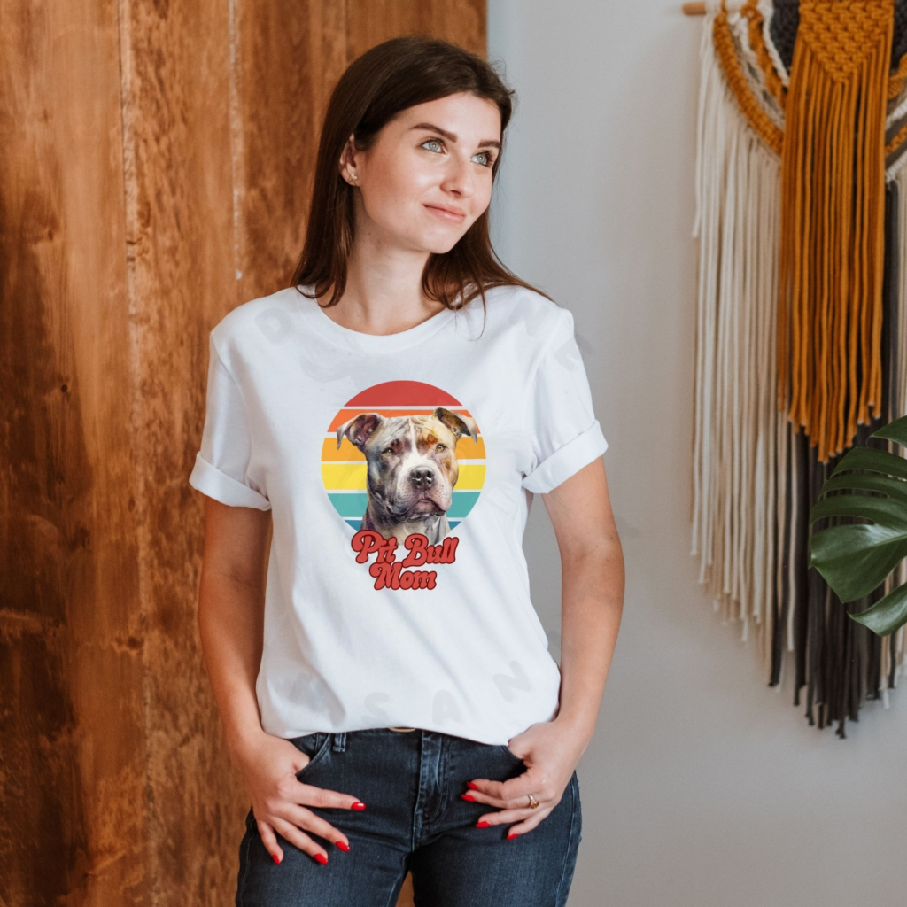 a woman wearing a white tee featuring a retro sunset design and a pit bull with the words pit bull mom in retro script