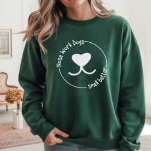 a woman with her hand in her pocket wearing a forest green crewneck sweatshirt that says nose work dogs smell better with a graphic of a dog's nose