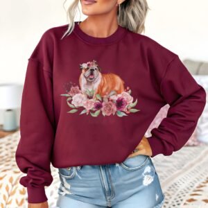 a woman standing in front of a bed wearing a maroon crewneck sweatshirt featuring an image of a English Bulldog in watercolor flowers