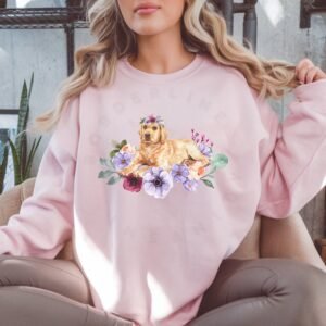 a woman on a sofa wearing a light pink crewneck sweatshirt featuring an image of a yellow lab in watercolor flowers