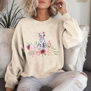 a woman on a sofa wearing a sand colored crewneck sweatshirt featuring an image of a dalmatian in watercolor flowers