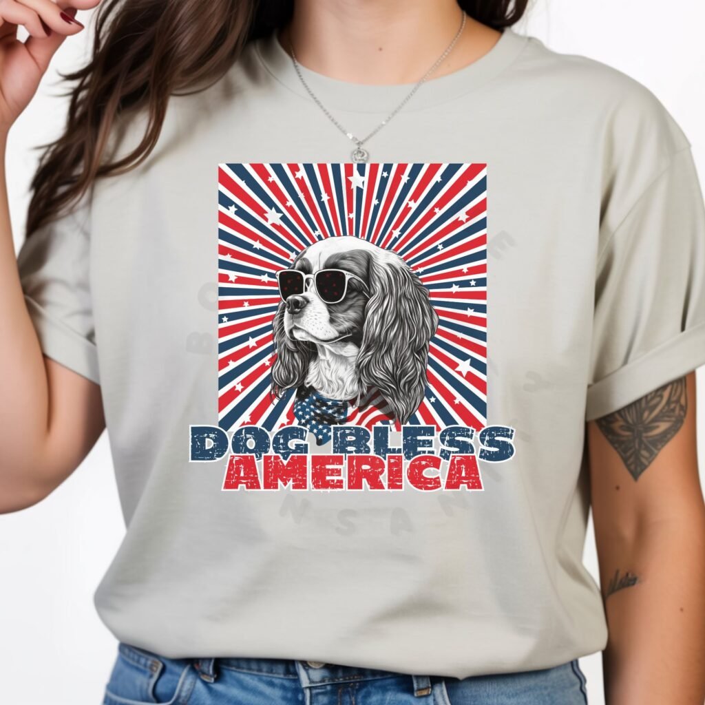 a woman wearing a silver tee with a patriotic background and an image of a cavalier in an american flag bandana and sunglasses that says dog bless america