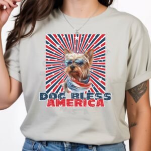 a woman wearing a silver tee with a patriotic background and an image of a Yorkshire Terrier in an american flag bandana and sunglasses that says dog bless america